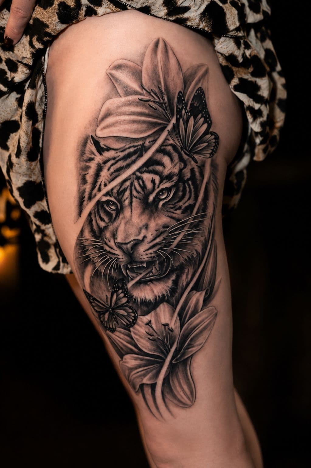 Tijgertattoo met lelies en vlinders op het bovenbeen, in ander licht gefotografeerd